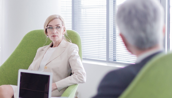 K21 A woman sitting in a green chair, listening attentively during a conversation with another person in a professional setting.