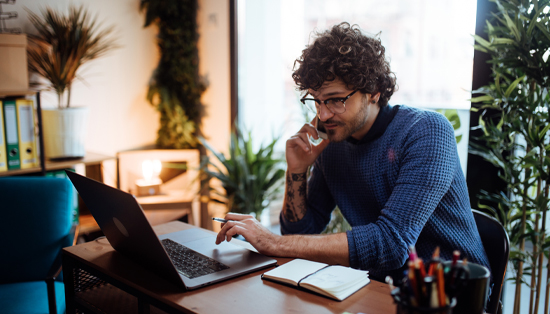 K22 A person working on a laptop while talking on the phone in a home office setting during the COVID-19 crisis.
