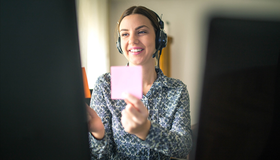 K23 A person smiling and holding a sticky note during a telehealth session, wearing a headset.