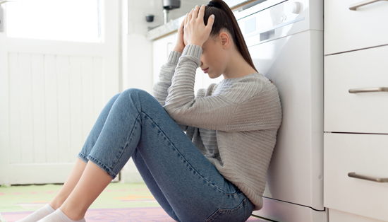 A person sitting on the floor, holding her head in distress, indicating emotional struggle during the COVID-19 pandemic.