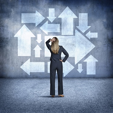 A businesswoman standing with her back to the camera, looking at arrows on a wall, symbolizing decision-making and uncertainty.
